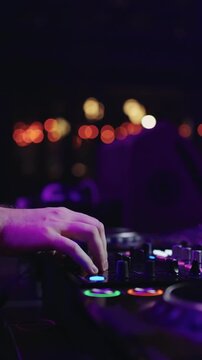 Close up of DJ hands adjusting mixer controls and performing live set on professional turntables with colorful club lights and blurred nightlife background