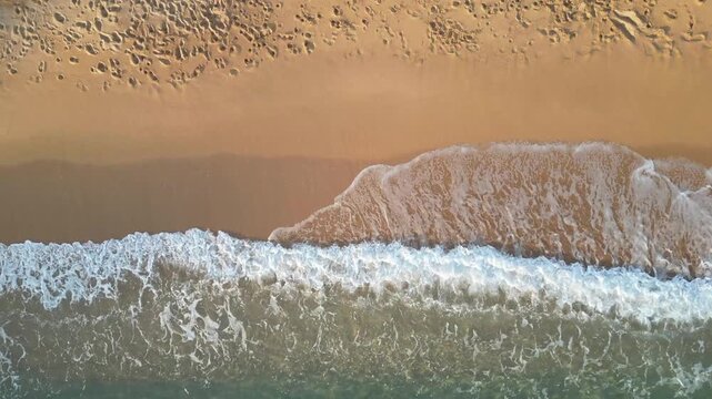Cenital aerial drone view of sea waves crashing on the shore, sand and foam on the coastline, 4k nature background