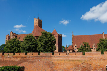 Panoramic view of Malbork Castle walls and towers with trees and historic buildings in background
