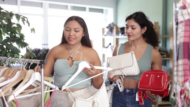 Girl client chooses dress or tank top, female assistant consultant offers to complement outlook wardrobe, purchase bag. Concept of seasonal fashion shopping