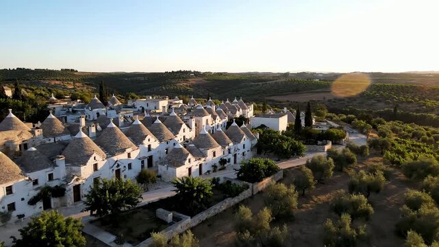 Drone aerial view of traditional Apulian trulli houses nestled in olive groves at sunrise