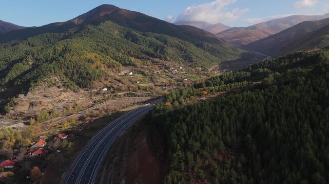 Aerial video of the A1 motorway winding through the mountain valleys of Mirdita, surrounded by autumn forests and scattered hillside homes in Northern Albania. 