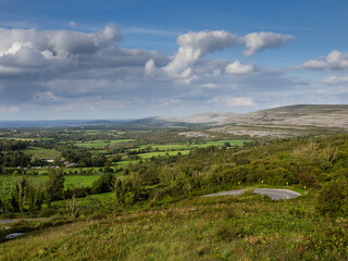 Fototapeta premium Landscape scene with green fields, hills, ocean and blue sky. Burren area, county Galway, Ireland. Warm sunny day. Rural Irish scenery in unique location. Travel and tourism.