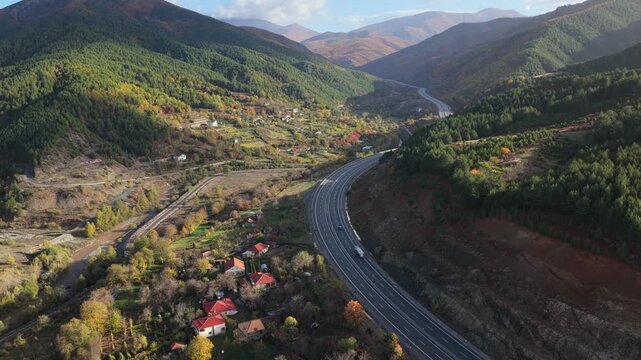 Aerial video of the A1 motorway winding through the mountain valleys of Mirdita, surrounded by autumn forests and scattered hillside homes in Northern Albania. 