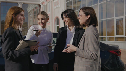 Group of women discussing business plans outside a building in the daytime while holding notebooks and tablets