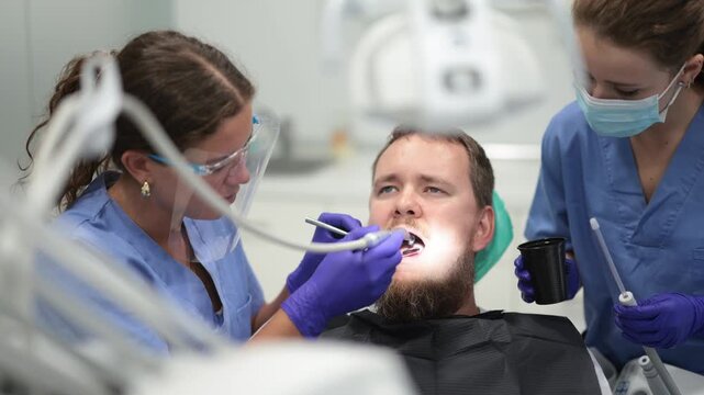 Two female dentists treat man teeth at a dental clinic. High quality 4k footage
