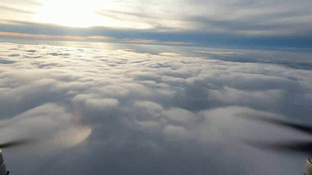 Scenic aerial view from a propeller plane flying over a beautiful sea of clouds at sunrise. First person perspective from the window.