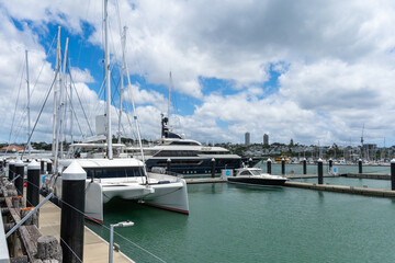 Fototapeta premium A collection of luxury yachts and motorboats moored at the bustling Viaduct Harbour with the modern Auckland CBD skyline in the background.