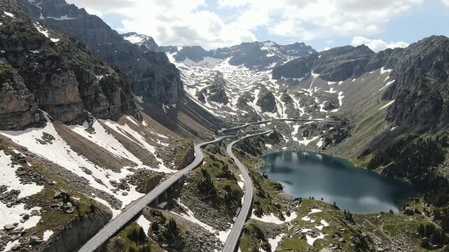 Spectacular aerial view of a winding mountain road and a serene alpine lake surrounded by snow-capped peaks