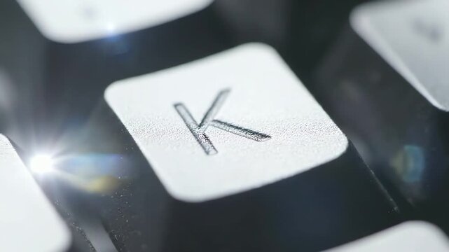Extreme close-up of a keyboard key with the letter K illuminated by soft light and lens flare
