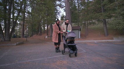 African American parents gently push a baby stroller while looking at their child, sharing warm family bonding outdoors during autumn with care, love and calm mood.