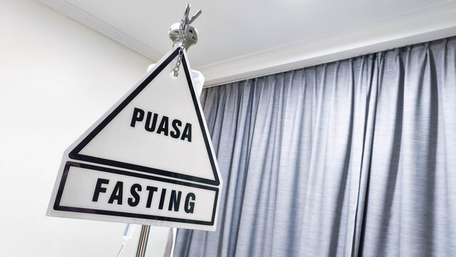 Hospital fasting sign labeled Puasa and Fasting hanging indoors, indicating patient medical instruction before treatment or surgery, representing healthcare communication, safety, and clinical prepara