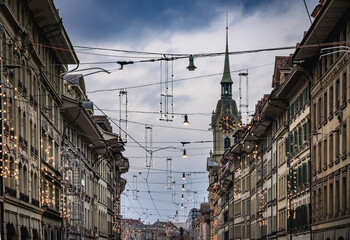 Golden clock tower above stone arcade with Christmas lights in Bern, Switzerland