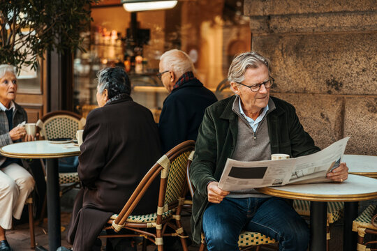 Senior man reading newspaper while spending leisure time in sidewalk cafe