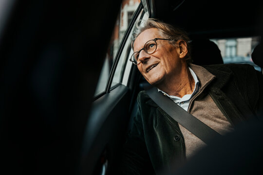 Curious smiling senior man looking out through window while traveling in car