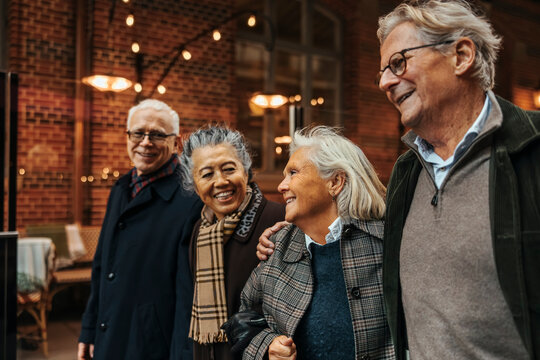 Smiling senior couple enjoying leisure time walking with friends at city street