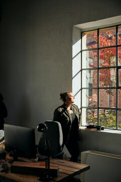 Female entrepreneur day dreaming while standing near window in startup office