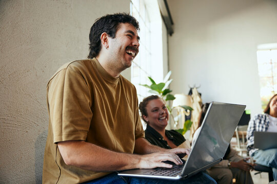 Happy male business entrepreneur sitting with laptop in tech office meeting
