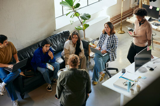 High angle view of male and female business experts listening to colleague sharing ideas in meeting at tech office