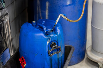 Blue industrial gas canister with flexible brass hose connection and hazard warning label in workshop setting