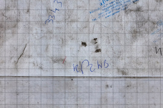 Detailed view of dirty graph paper with handwritten technical notes and calculations showing workshop documentation