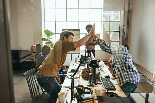 Happy male and female giving high-five to each other in office seen from glass