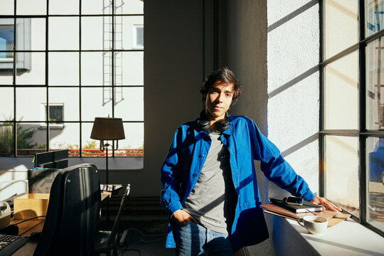 Portrait of confident young male entrepreneur with headphones around neck standing near window in office