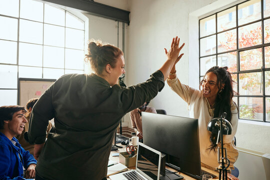 Cheerful female business expert giving high-five to colleague during meeting in tech office