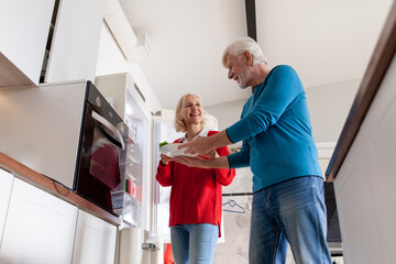 elderly couple uses refrigerator in the kitchen, gray-haired woman and her husband cook food in the kitchen and take vegetables from the refrigerator