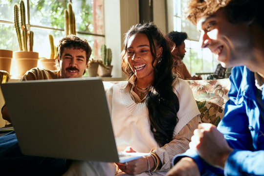 Happy female business expert using laptop while sitting with male colleagues in tech office