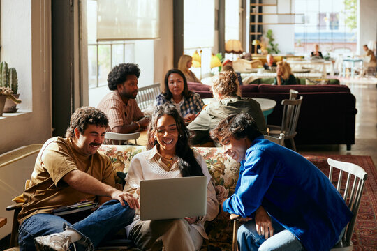 Smiling female business expert using laptop while sitting with male colleagues in tech office lobby