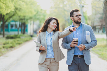 Two business colleagues walking in a park during a break, woman gesturing and pointing 