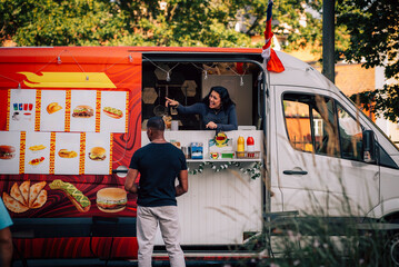 Happy saleswoman explaining menu to male customer while standing in food truck
