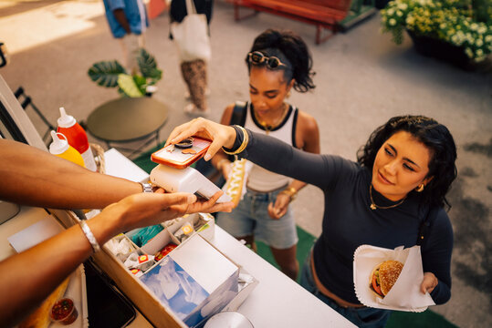 High angle view of woman scanning smart phone on credit card reader while buying snack at food truck