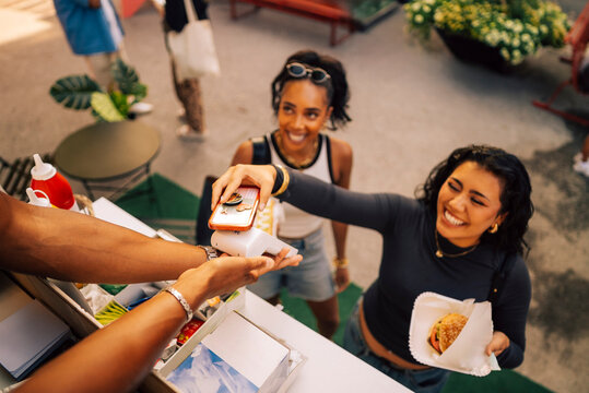 High angle view of smiling woman using tap to pay method while buying snack at food truck