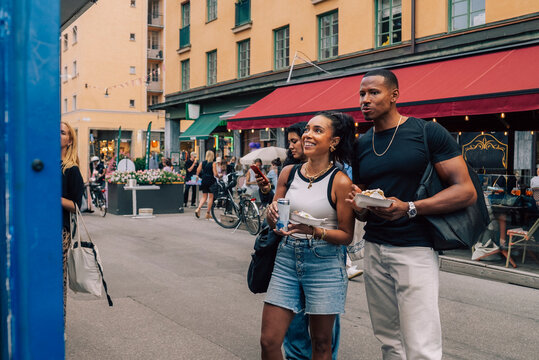 Male and female friend holding fast food looking at window display while standing on road