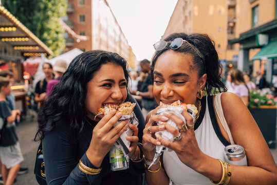 Multiracial female friends eating wrap sandwich while enjoying at food festival