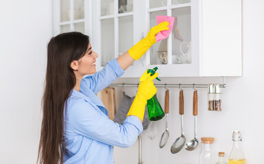Closeup portrait of smiling woman wearing protective rubber gloves cleaning cupboard surface in...