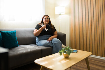 Young woman relaxes on a gray couch in her cozy living room, savoring a cup of coffee in her leisurely moments at home