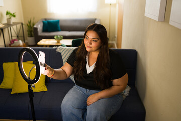 Plus size woman vlogging from home, creating social media content using ring light and smartphone