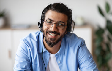 Call Center Operator. Closeup portrait of positive indian man customer service representative in headset, handsome western guy hotline manager looking at camera and smiling, selective focus