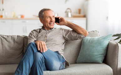 Happy Senior Man Talking On Mobile Phone Looking Aside Sitting On Couch At Home. Grandpa...