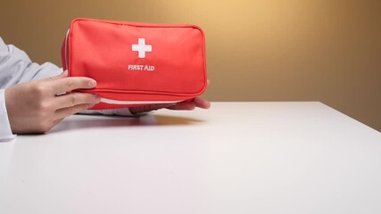 Doctor in a medical gown holding an orange first aid kit in outstretched hands over a white desk, emphasizing readiness for medical emergencies and health safety