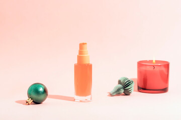 Cosmetic spray bottle with candle and Christmas ornaments on pastel pink background. Closeup