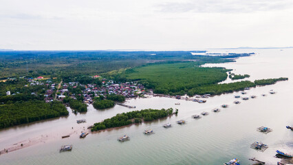 Aerial view of the Cerucuk River estuary flowing into the open sea in Tanjung Pandan, Belitung, Indonesia. Features lush mangrove forests, lines of floating fish cages, and a coastal fishing village.