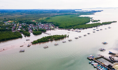 Aerial view of the Cerucuk River estuary flowing into the open sea in Tanjung Pandan, Belitung, Indonesia. Features lush mangrove forests, lines of floating fish cages, and a coastal fishing village.