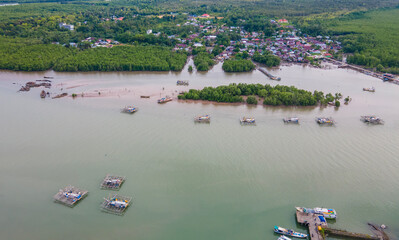 Aerial view of the Cerucuk River estuary flowing into the open sea in Tanjung Pandan, Belitung, Indonesia. Features lush mangrove forests, lines of floating fish cages, and a coastal fishing village.