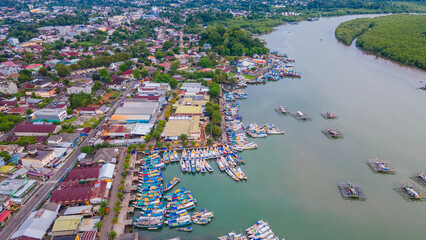 Drone view of Tanjung Pandan city and Cerucuk River in Belitung, Indonesia. The landscape shows a busy fishing harbor with traditional boats parked next to the urban settlement.