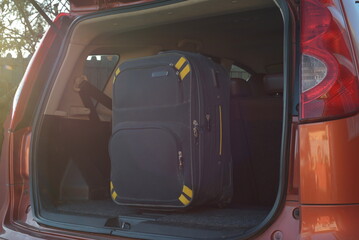 Large black suitcase with yellow accents standing upright inside the trunk of an orange car, ready for a trip. © esvetleishaya