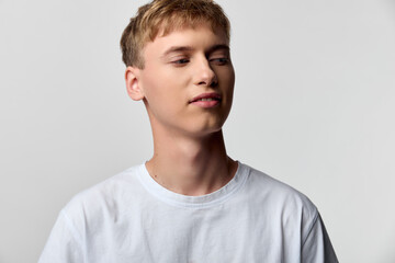 Young man in casual tshirt poses against neutral background, head tilted slightly, soft lighting,...